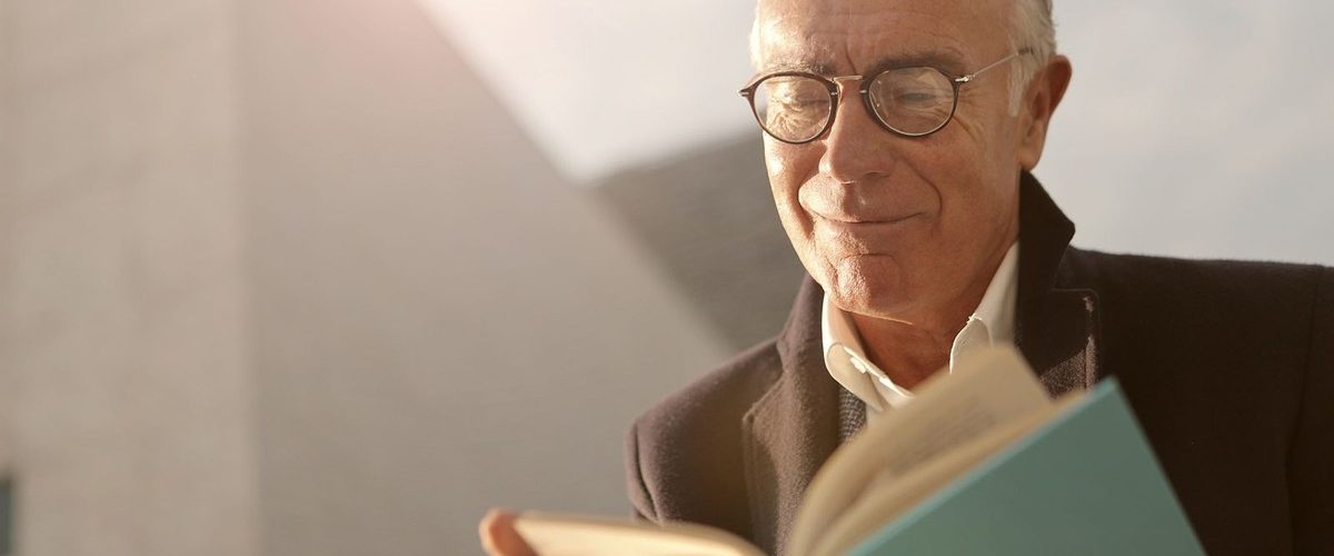 Hombre de mediana edad con gafas leyendo un libro, síntoma habitual de presbicia corregida
